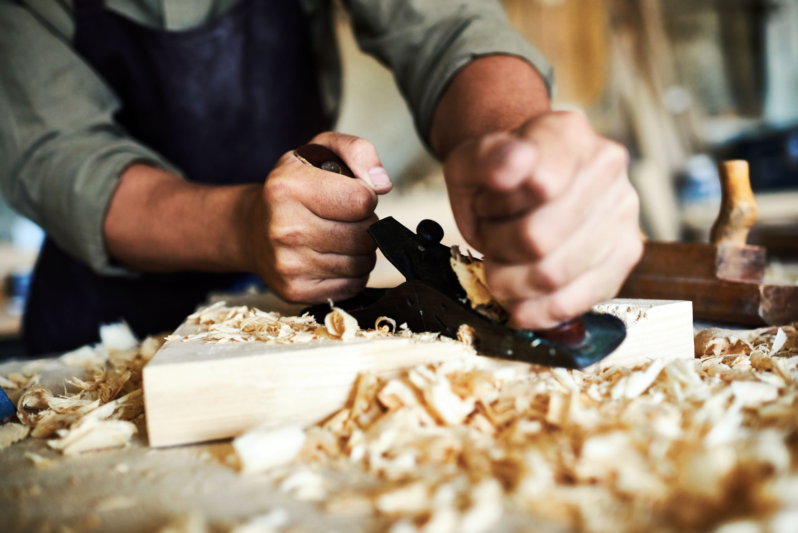 Closeup portrait of strong male hands shaving piece of wood with plane tool in carpenters workshop making furniture